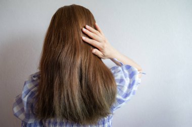 Ayakta duran ve kalın saçlarına dokunan Asyalı kadının dikiz görüntüsü. Kalın saç, saç yoğunluğu ve saç foliküllerinin sayısını ifade eder..