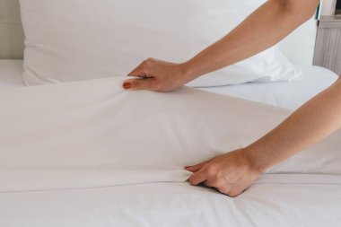 Otel hizmetçisinin kesilmiş fotoğrafı otel odasındaki battaniyeyi düzenliyor. Otel odasında yatak yapan kadın oda hizmetçisi kavramı..