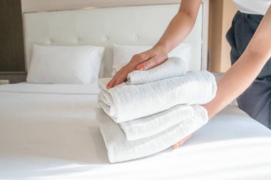 Otel hizmetçisinin yataktaki havlu yığınını düzenlerken çekilmiş bir fotoğrafı. Otel odasında yatak yapan kadın oda hizmetçisi kavramı..