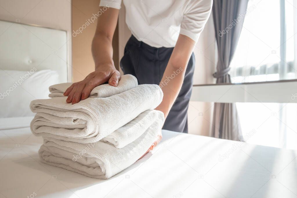 Cropped shot of hotel maid arranging the stack of towels on bed. Conceptual of female chambermaid making bed in hotel room.