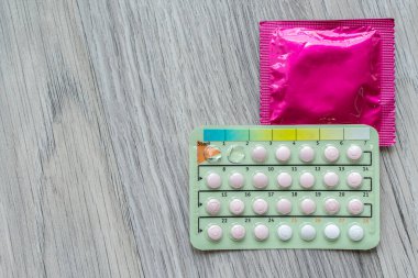 Tahta zeminde doğum kontrol hapları ve prezervatifler var. Hamileliği önlemek için kullanılan doğum kontrol nesneleri veya aygıtı kavramı.
