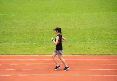 Stadyumdaki koşu pistinde koşan genç atlet kadının yan görüntüsü. Koşu pisti, atletizm için yapay bir koşu alanıdır..