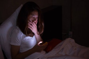 Bağımlı bir kadın gece geç saatlerde internette akıllı telefonuyla sohbet edip sörf yapıyor. Uykusuzluk ve seyyar bağımlılık kavramı.