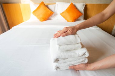 Otel hizmetçisinin yatağın üzerindeki havlu yığınını düzenlemesini kapat. Otel odasında yatak yapan kadın oda hizmetçisi kavramı..