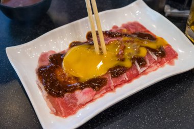 Shabu-Shabu restoranının tepesinde taze yumurtayla dilimlenmiş et. Yemek, masadaki lokanta tarafından parça parça pişiriliyor..