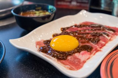 Shabu-Shabu restoranının tepesinde taze yumurtayla dilimlenmiş et. Yemek, masadaki lokanta tarafından parça parça pişiriliyor..