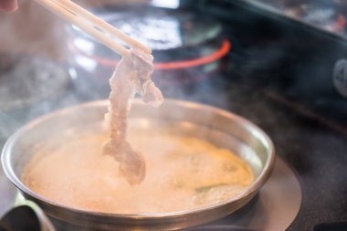 Geleneksel Japon yemeği Shabu-Shabu yemek için çubuk kullanan birine yakın çekim. Dilimlenmiş et ve sebzeler suda kaynatılır ve sosla servis edilir..