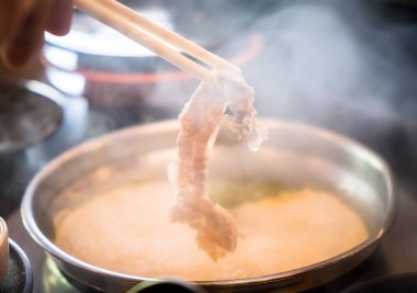 Geleneksel Japon yemeği Shabu-Shabu yemek için çubuk kullanan birine yaklaş. Dilimlenmiş et ve sebzeler suda kaynatılır ve sosla servis edilir..