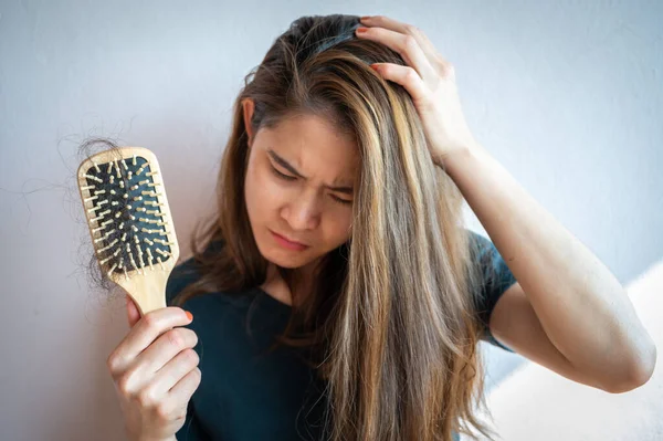 Worried woman holding comb with hair loss after brushing her hair. Hair loss it cause from family history, hormonal changes, unhealthy of aging.