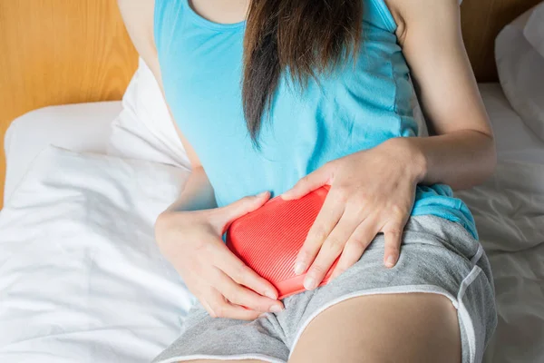 Adet döneminde karnına kramp giren genç bir kadın acıya karşı sıcak su şişesi tutuyor..