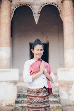 Laos 'un kuzey merkezindeki UNESCO dünya mirası alanı Luang Prabang' daki eski tapınağın önünde selamlaşan geleneksel Laos kıyafetleri giyen Asyalı bir kadının portresi..