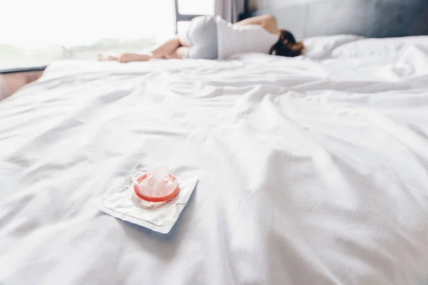 女人在床上睡觉时 撕破放在床上的小避孕套 安全性行为和防止怀孕的概念 — 图库照片