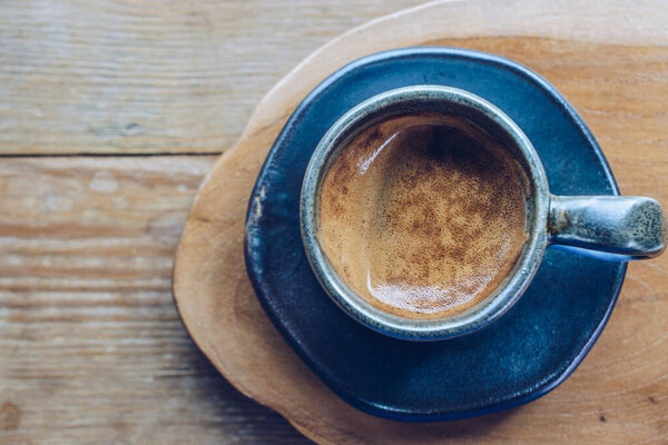 A cup of hot espresso shot on the wooden table. Espresso is a full-flavored It is made by forcing pressurized, hot water through very finely ground coffee beans.