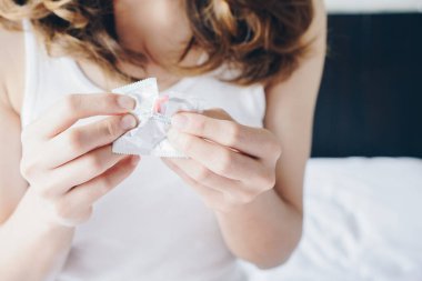 Partneriyle kullanmadan önce prezervatif ambalajını yırtan kadını yakından çek. Güvenli seks ve hamileliği önleme kavramı.