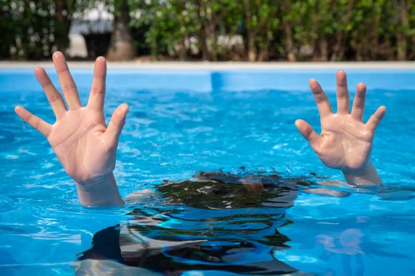 Woman showing her hands while drowing in swimming pool. Drowning is the process of experiencing respiratory impairment from submersion or immersion in liquid.
