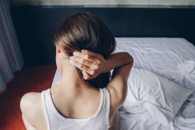 Genç Asyalı bir kadının yatakta oturup boyun ağrısı çekmesi ve sabah uyandıktan sonra vücudunu esnetmesi..