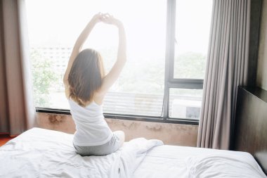 Back view of woman raised hands up and stretching in bed after waking up in the morning, start a new day with happiness.