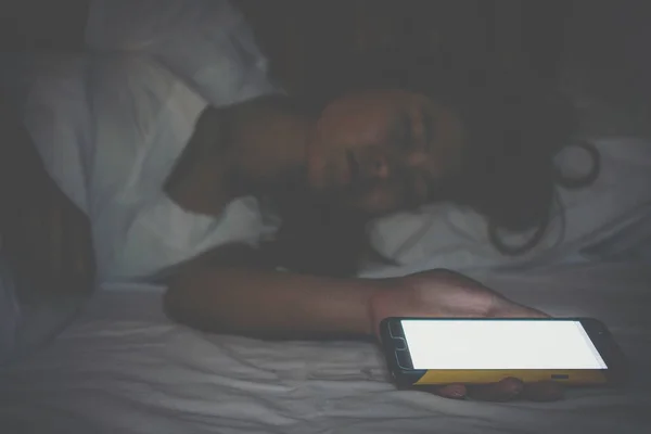 Woman sleeping on bed with her cell phone on night stand. Every person surrounded by technology even late at night.
