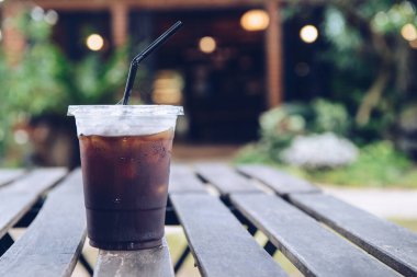 A plastic cup of iced Americano (black coffee) serving on the wood plank table. The Iced Americano is a simple classic made with espresso, water and ice.