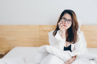 Portrait of young Asian sexy woman wearing white shirt and waiting for someone on the bed in hotel bedroom. Conceptual of woman lifestyle.