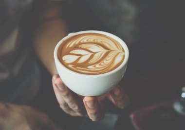 Close up of Barista holding a cup of coffee with latte art. Latte is a coffee drink made with espresso and steamed milk.