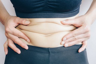 Close-up of Woman touching her fat belly, woman's hand holding excessive belly fat. Being overweight is one of the leading causes of major diseases such as heart disease, stroke, high blood pressure.