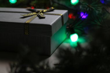 Çam ağacında altın kurdeleli defocus grisi hediye ya da köknar ağacı gece parıldayan yeşil, kırmızı ve mor ampullü bulanık arkaplan. Noel hediyesi. Tatil kutusu. Odaklanamıyorum.
