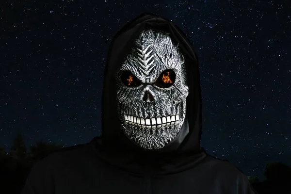 Close-up portrait of grim reaper. Man in death mask with fire flame in eyes on night sky starry. Carnival costume, creepy teeth. Halloween holiday concept. Dark horror.