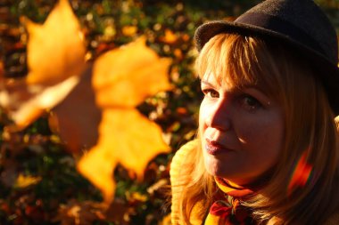 Renkli bir sonbahar parkında beyaz saçlı genç bir kadının yakın plan portresi. Turuncu sonbahar arka planında şapkalı, şık bir kadın. Mutlu sonbahar rüya konsepti. Bulanık sarı akçaağaç yaprağı.