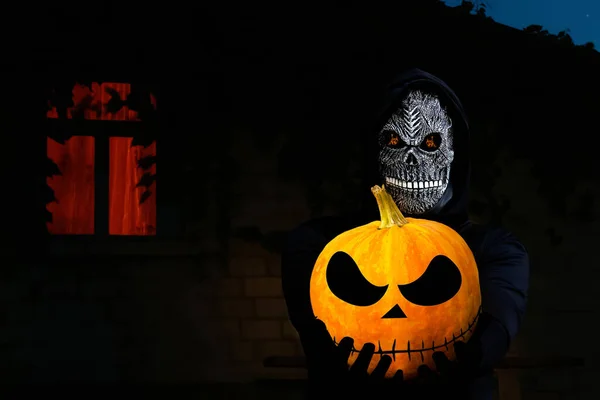 Close-up portrait of grim reaper. Man in death mask with fire flame in eyes on dark night background. Carnival costume, creepy teeth. Halloween holiday concept. Dark horror.