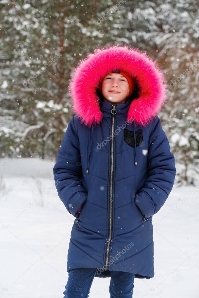 Vertical portrait of preteen girl in bright pink warm hood outside on nature winter snowy forest background. Pretty child smiling outdoor, cold weather. Caucasian kid 10 years. Happy vacations.