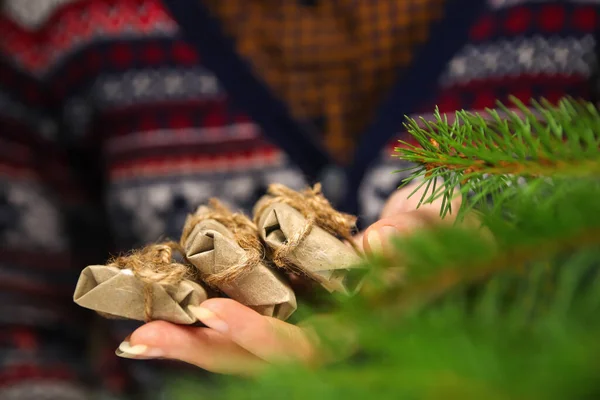 3つの小さな工芸品の贈り物を持つ女性の手 3有機ギフト ロープ弓を保持クリスマスセーターの若いヒップスター女性 居心地の良い暖かい冬の詳細 緑の自然前景 — ストック写真