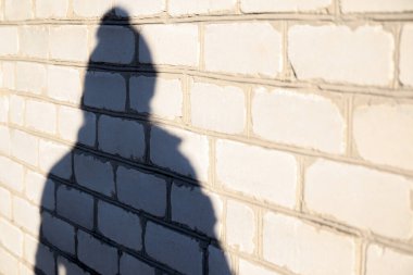 Beyaz tuğla duvarda kış şapkası takan birinin gölgesini yok et. Aydınlık ve gölge kadınlar. Kadın silueti var. Evin duvarında, dışında, dışında yansıması olan insanlar..