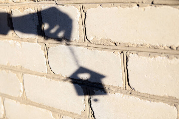 Defocus shadow of hand with Christmas toy small house on white brick wall. Light and shadow toy. House shadows with reflection on the house wall, outdoor, outside.