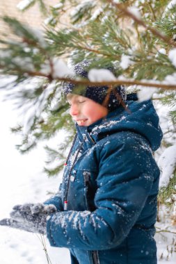 Kış ormanlarında kar fırtınasında gülümseyen çocuk. Karlı kış arka planında ağacın yanında duran gülümseyen çocuk. Aktif olarak dışarıda zaman geçirmek. Kar fırtınasında soğuk soğuk hava. Odaklanamıyorum