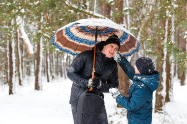 Kırsal kesimdeki karlı arka planda şemsiye tutan ve kavga eden genç adam ve komik çocuk. Mutlu aile, soğuk hava. Yaşam tarzı. Tatiller. Karlı kış, ormanda kayboldu. Baba ve oğul. Gülümsüyor