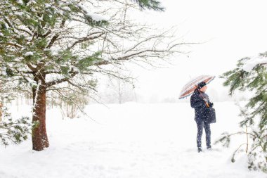 Sıcak şapkalı genç adam kırsal arka planda şemsiye tutuyor. Yeni yüzyılın kutlu olsun. Açık hava, soğuk hava. 20-25 yaşlarında beyaz bir adam. Karlı kış, ormanda kayboldu. Dışarıda.