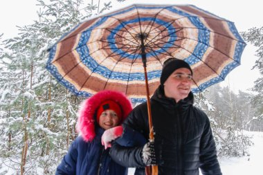 Young man and funny child girl on rural winter snowy background holding umbrella. Happy family, cold weather. Lifestyle. Vacations. Snowy winter, lost in forest. Older brother. Smiling.