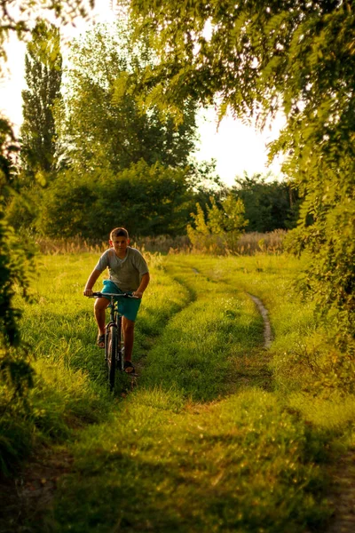 Bonne enfance. Un beau adolescent fait du vélo dans le sentier de la campagne. Nature vert prairie d'été fond. Enfant actif, mon enfant. Verticale. Concept sportif — Photo