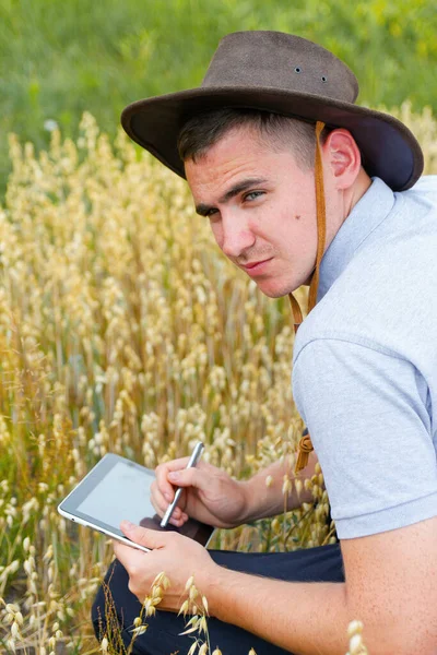 디지털 타블렛 농부의 카우보이 모자를 젊은이 밭에서 작물을 조사하고 있습니다 — 스톡 사진