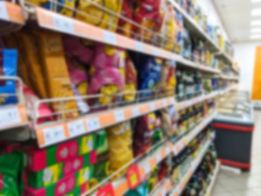 Defocus süpermarket koridoru ve raflar patates cipsi ile bulanık arka plan. Renkli raflarla dolu bulanık bir süpermarket koridoru. Perakende konsepti. Odaklanamıyorum.
