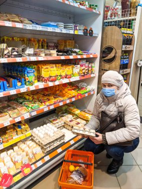 Volodymyr, Ukrayna - 13.02.2022: kadın süpermarkette yumurtaları farklı ürünlerle seçiyor. Renkli raflarla dolu süpermarket koridoru. Perakende kavramı.