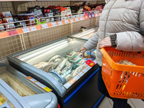 Volodymyr, Ucrânia - 13.02.2022: mulher segurando fundo cesta de supermercado com diferentes produtos e de pé perto da geladeira. Supermercado corredor prateleiras coloridas de mercadorias. Pessoa, pessoas — Fotografia de Stock