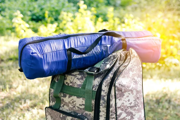 Defocus military backpack and blue tent or sleeping bag. Army bag on green grass background near tree. Military camouflage army rucksack. Tourist summer hiker. Sunny. Close-up. Outdoor. Out of focus.