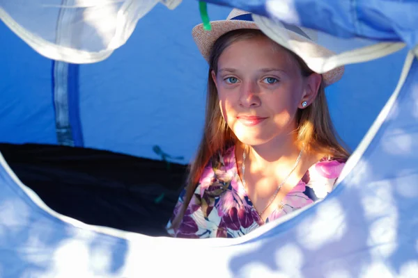 The girl sitting comfortably inside a camping blue tent behind a mesh anti-mosquito window, she looking outside. Portrait teen girl in hat. Morning. Travel kid. Sunflare. Relax, rest. Out of focus — Foto de Stock
