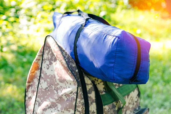 Askeri sırt çantası ve mavi çadır ya da uyku tulumu. Ağacın yanındaki yeşil çimlerin üzerinde ordu çantası. Askeri kamuflaj ordu sırt çantası. Turist yaz yürüyüşçüsü. Güneş parlaması. Yaz. Odaklanamıyorum