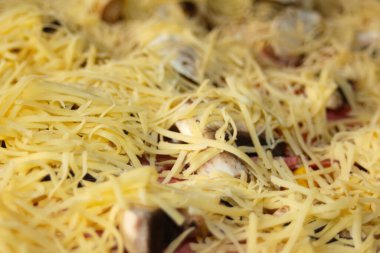 Defocus closeup round whole pizza with freshly grated mozzarella cheese on top. Defocus blurred ingredients for pizza on dough. Homemade yellow italian pizza. Italian cuisine background. Out of focus.