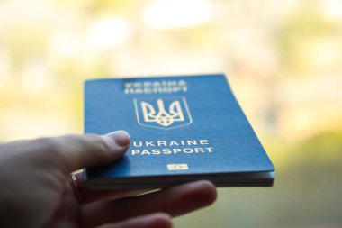 Bir Ukrayna vatandaşının bulanık bir şehir geçmişindeki kadın elinin defocus pasaportu, yakın plan. Ukrayna Ukrayna pasaportuyla yazılmış. - Savaş. İnsan, millet. Sınır kavramı. Yakınlaştır, odaktan çık.