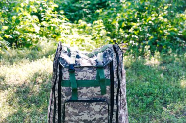 Askeri sırt çantasından çık. Ağacın yanındaki yeşil çimlerin üzerinde ordu çantası. İngiliz ordusunun sırt çantasında askeri kamuflaj malzemesi. - Yakın çekim. Turist yaz yürüyüşçüsü. Trip konsepti. Odaklanamıyorum.