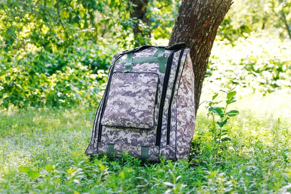 Askeri sırt çantasından çık. Ağacın yanındaki yeşil çimlerin üzerinde ordu çantası. İngiliz ordusunun sırt çantası ve sırt çantasında askeri kamuflaj ağı malzemesi. Turist yaz yürüyüşçüsü. Seyahat konsepti. Odaklanamıyorum.
